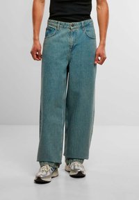 Lyseblå vide jeans med høy midje, fork pockets og synlig søm, kombinert med grå og hvite joggesko.