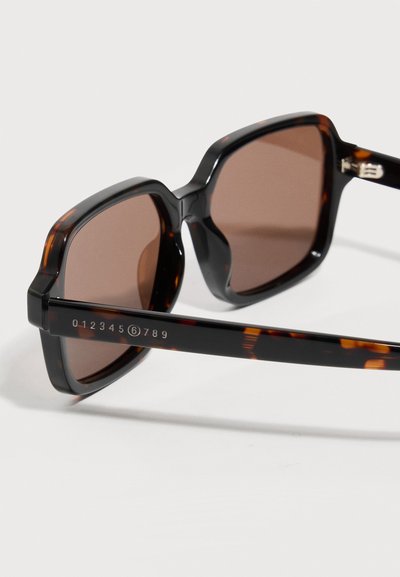 Square tortoiseshell sunglasses with brown lenses showing a novel numeric design on the arm from 0 to 9 with 6 circled.