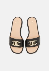 Sandales ouvertes en cuir noir à enfiler avec détail chaîne dorée et semelles intérieures beiges marquées "Aigner" sur fond blanc.