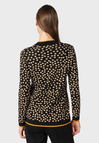 Maglione nero con un motivo a pois beige, con bordi arancioni a contrasto e maniche lunghe. Tessuto a maglia strutturato.