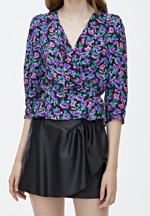 Mujer vistiendo una blusa envolvente de estilo floral en tonos púrpura y rosa, con mangas de tres cuartos, y una minifalda asimétrica de cuero sintético negro.