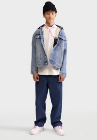 Denim jacket, light blue, with white graphic t-shirt underneath. Dark blue jeans and white sneakers with pink accents. Black beanie.