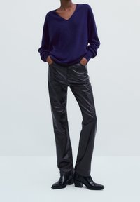 Pull en V bleu marine, à manches longues, coupe décontractée. Pantalons en faux cuir noir, coupe slim, poches avant. Bottines noires à talon large.