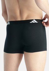 Svarta boxerkalsonger med en åtsittande passform, med en elastisk midja med vit Adidas-logotyp. Slät textur och minimala sömmar.