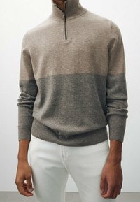 Knit pullover in light brown, featuring a gray band at the midsection, high collar with a quarter-zip. Soft texture and fitted sleeves.