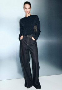 Czarny top z długim rękawem i drapowanym dekoltem, zestawiony z ciemnoniebieskimi spodniami o szerokich nogawkach z przednimi kieszeniami i kontrastowym przeszyciem.