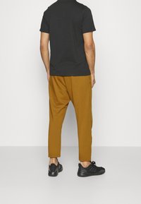Zwarte T-shirt met korte mouwen in combinatie met mosterdkleurige broek. De broek heeft een losse pasvorm en taps toelopende enkels. Zwarte sportschoenen maken de look compleet.