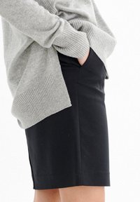 Pull en tricot gris avec des poignets côtelés, porté sur une jupe noire ajustée dotée de poches latérales et d'une texture lisse.