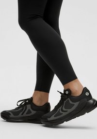 Sorte sportsko med mesh-detaljer, rund tå og fleksible såler. Har et kontrasterende tekstureret mønster og snøringer. Velegnet til sport.