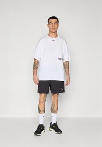 T-shirt branca de manga curta com logótipo preto, combinada com calções desportivos pretos, ténis pretos e meias brancas com detalhes pretos.