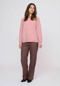 Maglione rosa lavorato a maglia con maniche lunghe e scollo rotondo, abbinato a pantaloni a scacchi marroni e scarpe nere a punta.