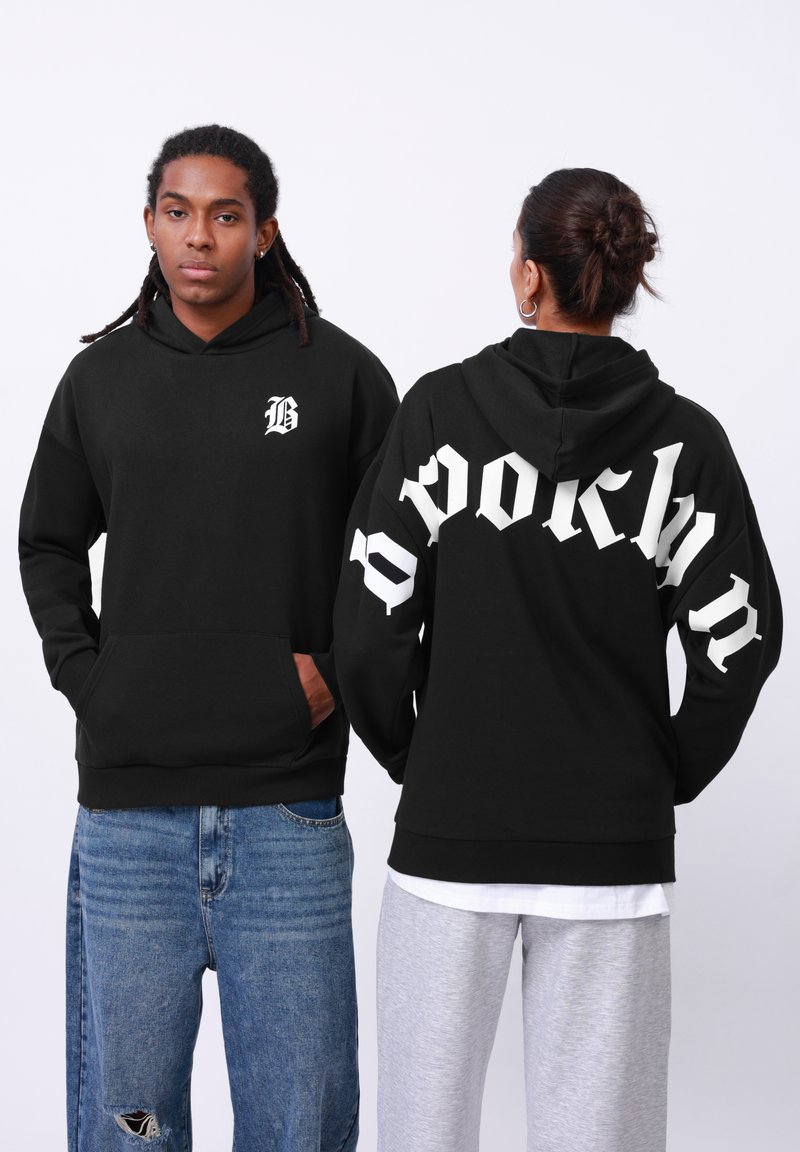 Sweat-shirt à capuche noir avec un petit "B" blanc sur le devant et "BROOKLYN" en grandes lettres blanches au dos. Tissu en mélange de coton.