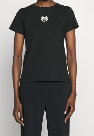 Person iført en ensfarvet sort t-shirt med korte ærmer og et lille hvidt rundt logo centreret nær halsudskæringen.