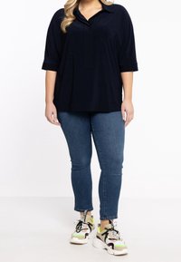 Marinekravebluse med korte ærmer, parret med slim-fit blå jeans og multicolore sneakers med sorte detaljer og snørebånd.