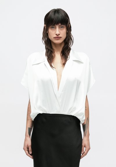 Witte satijnen blouse met diepe V-hals en korte mouwen, gecombineerd met een zwarte rok met hoge taille. Soepele textuur, op maat gesneden pasvorm, minimalistische stijl.