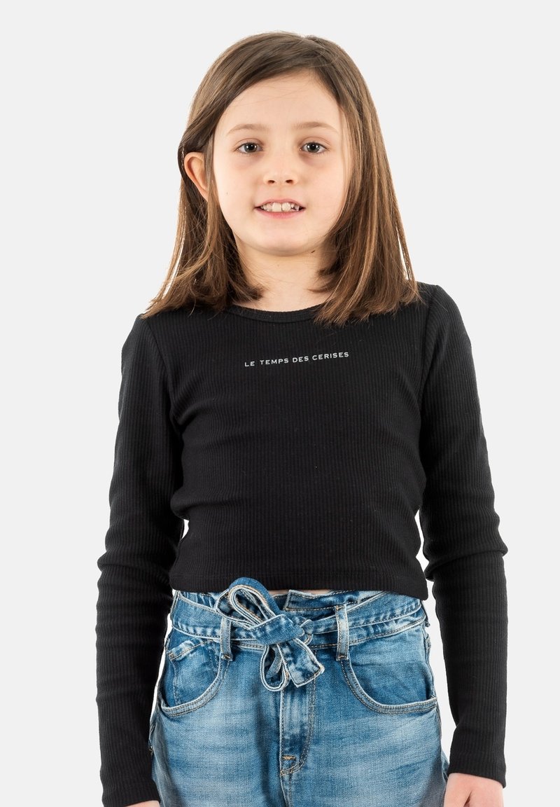 Haut à manches longues noir côtelé avec texte blanc, associé à un jean en denim bleu délavé avec une ceinture nouée à la taille.