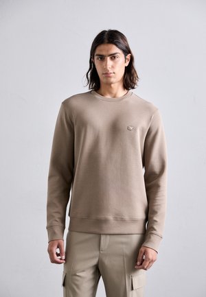 Brun sweatshirt med rund halsringning, långa ärmar och ribbade muddar. Har en liten, hexagonal logotyp på bröstet. Mjuk textur och figurnära design.