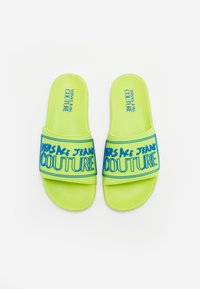 Infradito verde neon con una fascia larga, caratterizzate dal testo blu "VERSACE JEANS COUTURE". Design piatto con una soletta testurizzata.