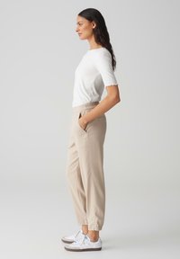 Beige, taperende joggers met een elastische tailleband en zakken, gecombineerd met een wit, kort mouwtopje met een geschulpte halslijn. Witte sneakers.