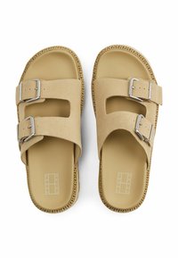 Sandalias beige con dos hebillas ajustables, correas de ante suave y una suela de goma lisa. Presenta un detalle de costura a lo largo del borde.