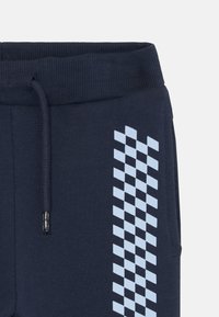 Pantalones jogger azul marino con patrón a cuadros azules en el costado, cinturilla elástica con cordón, fabricados en una tela suave y texturizada.