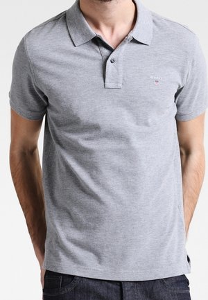 Polo grigio con una consistenza morbida, maniche corte e un pattino con due bottoni. Presenta un piccolo logo sul lato sinistro del petto. Tessuto elasticizzato.