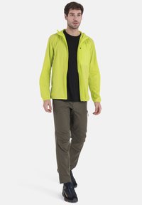 Lightweight lime green jacket with hood, black top, olive pants, and black footwear. Features zippers and subtle textures. Suitable for outdoor activity.