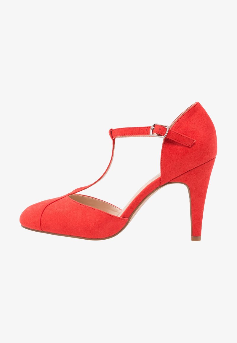 Chaussure Mary Jane en daim rouge à talon moyen avec bride en T et fermeture à boucle argentée, bout arrondi et talon fin sur fond blanc.