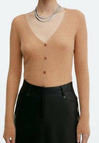 Žebrovaný kardigan s dlouhým rukávem v světle hnědé barvě, s hlubokým výstřihem do V, zapínáním na knoflíky a přiléhavým střihem. Vůbec neformálně v kombinaci s černou koženou sukní.