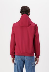 Sweatshirt vermelho com gola alta, punhos e cós elásticos. Apresenta uma textura suave e detalhes de costura discretos. Usado com jeans azuis.