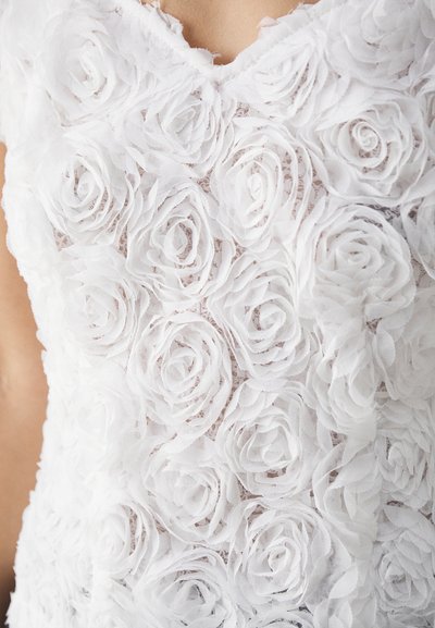 Weißes ärmelloses Oberteil aus strukturiertem Stoff mit geschichteten, blumenartigen Applikationen, die Rosen ähneln, mit einem gewellten Ausschnitt und aufwendigen Details.