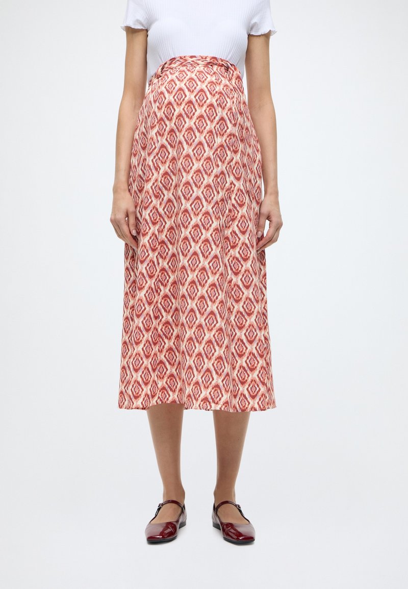 Jupe midi à motifs rouges et blancs, présentant un design en losanges, une coupe évasée et un tissu lisse. Associée à des chaussures bordeaux brillantes.