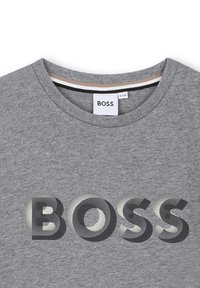 Grijze katoenen T-shirt met een ronde halslijn. Heeft een groot "BOSS" logo in zwart met een grijs stippenpatroon over de borst.