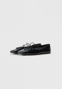 Scarpe flat in pelle nera con punte appuntite, occhietti decorativi e dettagli in pizzo sulla parte superiore, su uno sfondo bianco semplice.