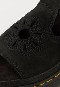Sandale din suede negru cu un design decupat floral, suprafață texturată și o cusătură galbenă contrastantă la talpă. Design cu vârf și călcâi deschis.