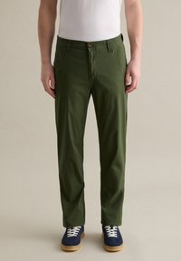 Groene katoenen broek met een rechte snit, voorzien van een knoopsluiting en zijzakken, gecombineerd met blauwe sneakers en witte veters.