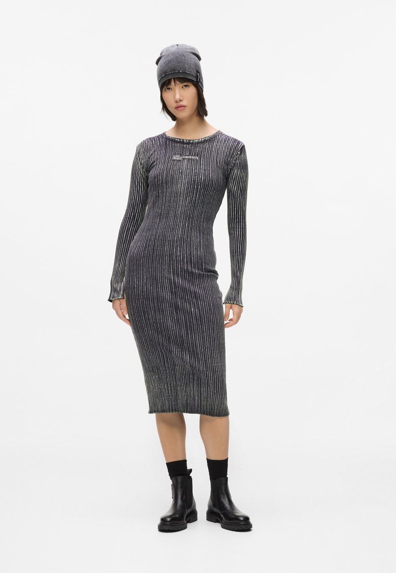 Vestido de manga larga, ajustado, en negro con rayas plateadas horizontales, con cuello redondo y textura acanalada. Combinado con un gorro de punto gris.
