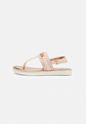 Light pink sandal featuring a textured strap, gold accents, and a contrasting white sole with ridges for grip. Adjustable ankle strap included.
