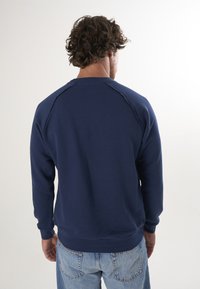 Granatowy sweter z okrągłym dekoltem, raglanowymi rękawami i ściągaczami. Miękka tekstura, minimalistyczny design, pokazany z tyłu, w połączeniu z jasnymi dżinsami.