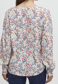Blumenbluse mit cremefarbenem Hintergrund und roten, blauen und grünen Blumen. Lange Ärmel mit gerafften Manschetten und rundem Halsausschnitt.