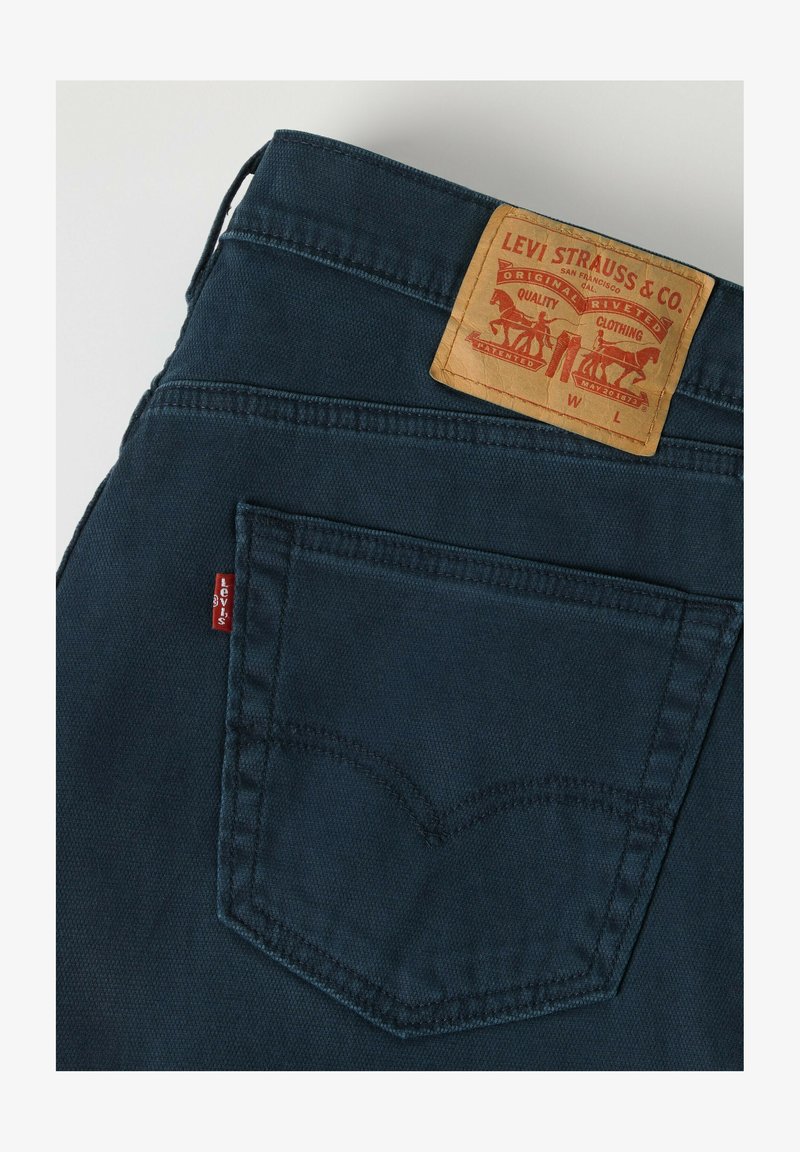 Baglomme på mørkeblå Levi's jeans med lædermærke og rød Levi's stofmærke på lommesømmen.