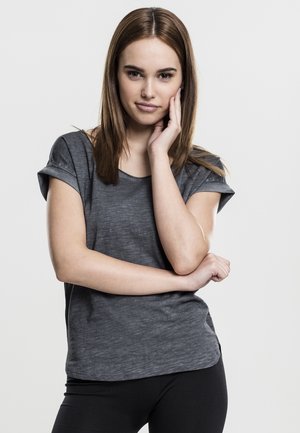 Grå T-skjorte med korte ermer og avslappet passform, myk tekstur og lett rullede ermer, paret med svarte tettsittende leggings.