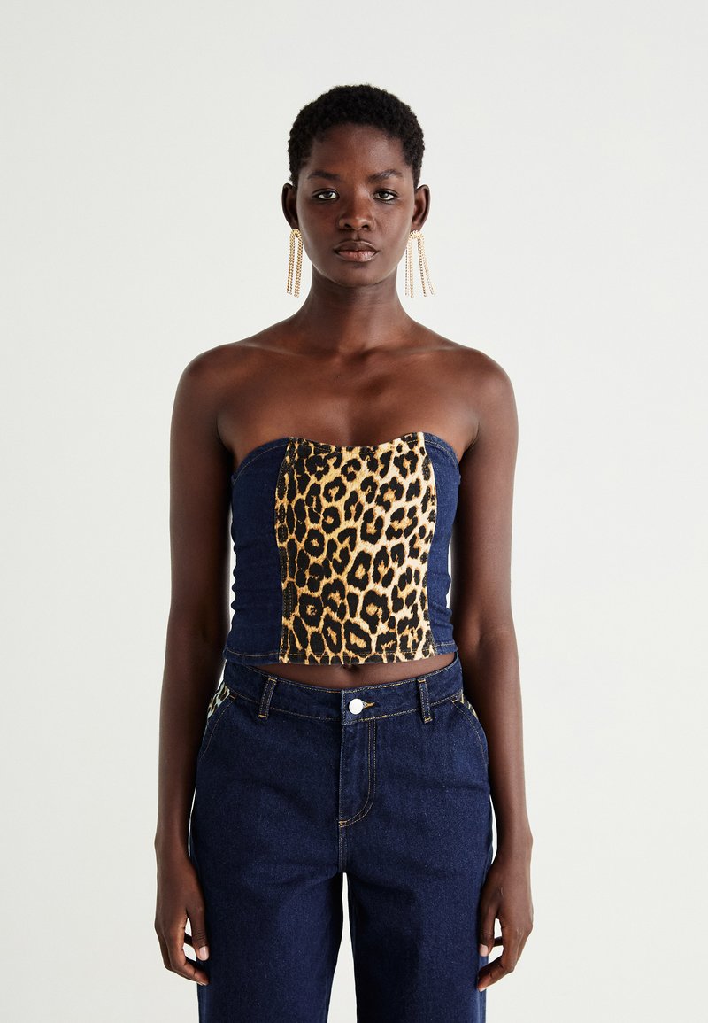 Bezdidelis viršus su leopardinėmis raštais priekyje ir tamsiai mėlyna džinsine nugarėlė, pasižymintis prigludusia forma ir siuvinėjimo detalėmis. Užsivilkta su tamsiai mėlynais džinsais.