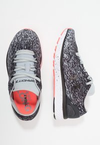 Scarpe da ginnastica grigie con una tomaia a fantasia, dotate di lacci grigi chiari, accenti corallo e una suola bianca e nera con macchie.