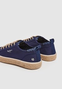 Námořnické plátěné tenisky s jutovými podrážkami, s béžovými tkaničkami a modrým vzorovaným akcentem na patě. Logo na vnější straně.