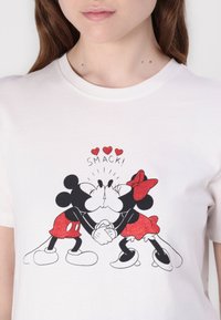 White t-shirt featuring a graphic of Mickey and Minnie Mouse kissing, with red glitter accents and "SMACK!" text above them.
