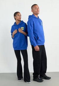 Blue hooded sweatshirts with front pockets, yellow "COOL KIDS" text on the left side, paired with black flared pants and shoes.