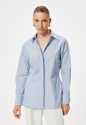 Camisa abotonada de color azul claro con rayas rojas verticales, de mangas largas y con un collar clásico. Textura de tela suave con un corte ajustado.