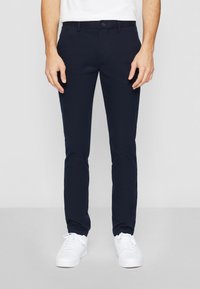 Marineblauwe chino's van stretchkatoen met een slim fit, voorzien van zijzakken en een knoopsluiting, gecombineerd met witte sneakers.