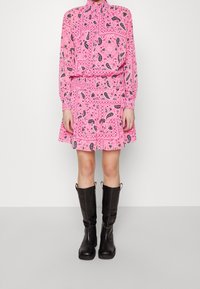 Robe rose ornée de motifs cachemire noirs, avec un col montant et des manches longues, associée à des bottes noires montantes jusqu'aux genoux.